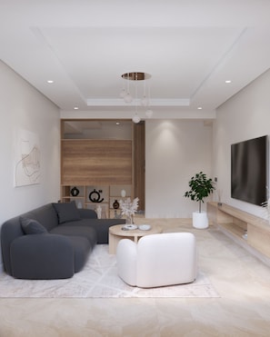Ein modernes Wohnzimmer mit einem Ecksofa, einem runden Couchtisch und einem großen Flachbildfernseher an der Wand.