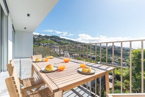 Una tavola di legno apparecchiata per la colazione su un balcone con vista panoramica su una cittadina collinare.