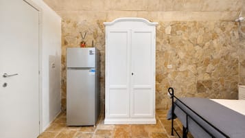 Een kleine kamer met een witte kast, een kleine koelkast en een bed met metalen frame.