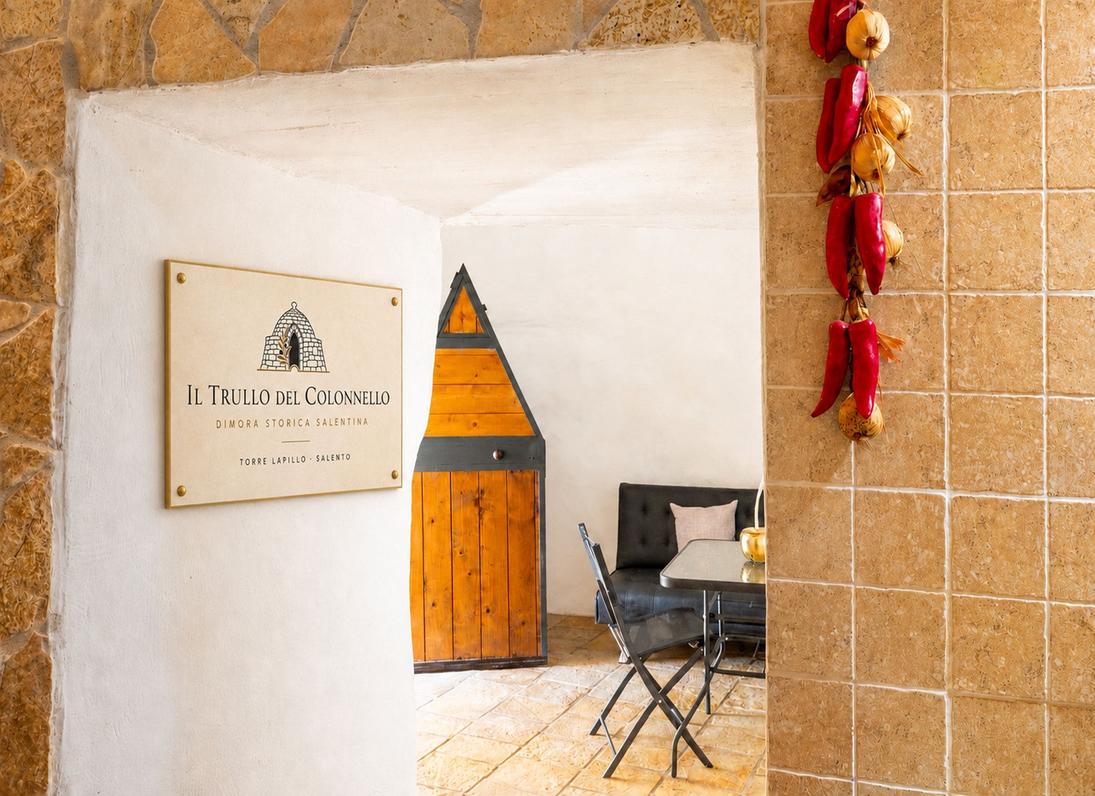 A room with a wooden door, a framed sign, a table with a chair, and decorative peppers on the wall.