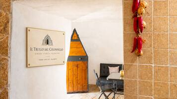 A room with a wooden door, a framed sign, a table with a chair, and decorative peppers on the wall.