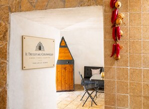 A room with a wooden door, a framed sign, a table with a chair, and decorative peppers on the wall. - The Trullo Privè - Porto Cesareo Private Retreat (Porto Cesareo)