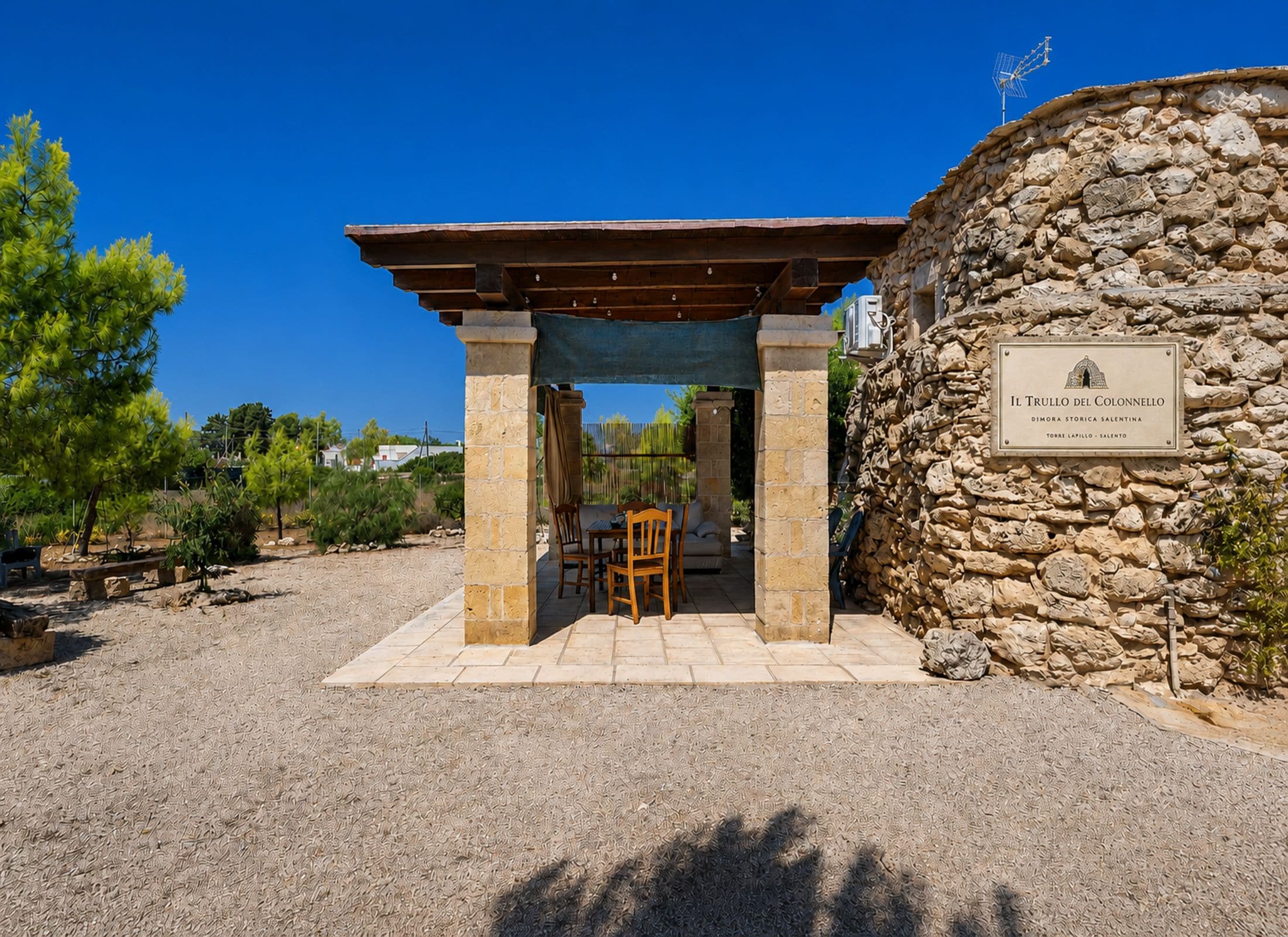 A stone building with a pergola entrance, a stone wall with a plaque, and outdoor seating.