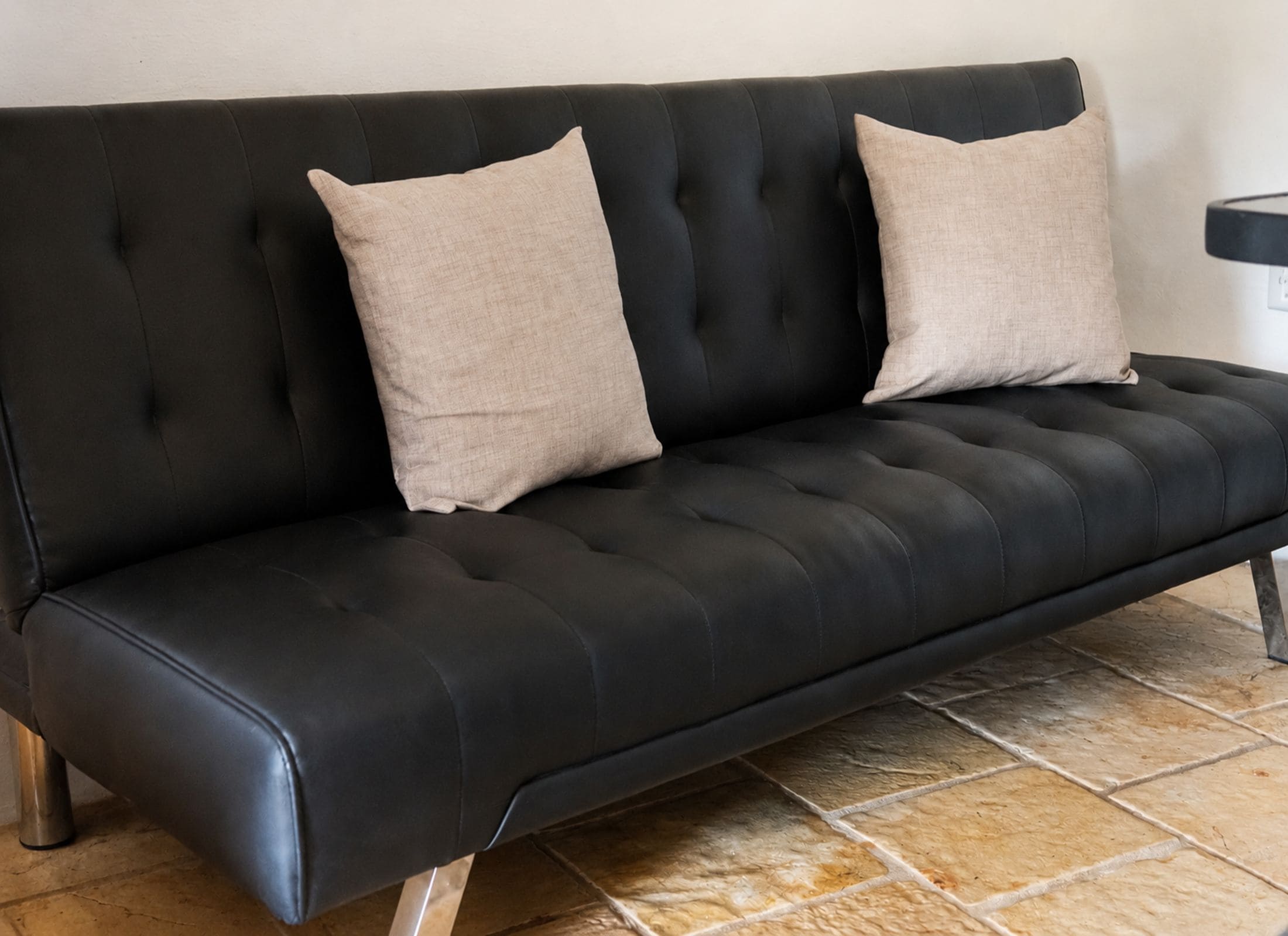 Un sofá de cuero negro con dos cojines color beige frente a una pared lisa.