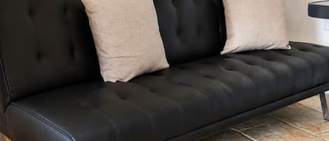 Un sofá de cuero negro con dos cojines color beige frente a una pared lisa.