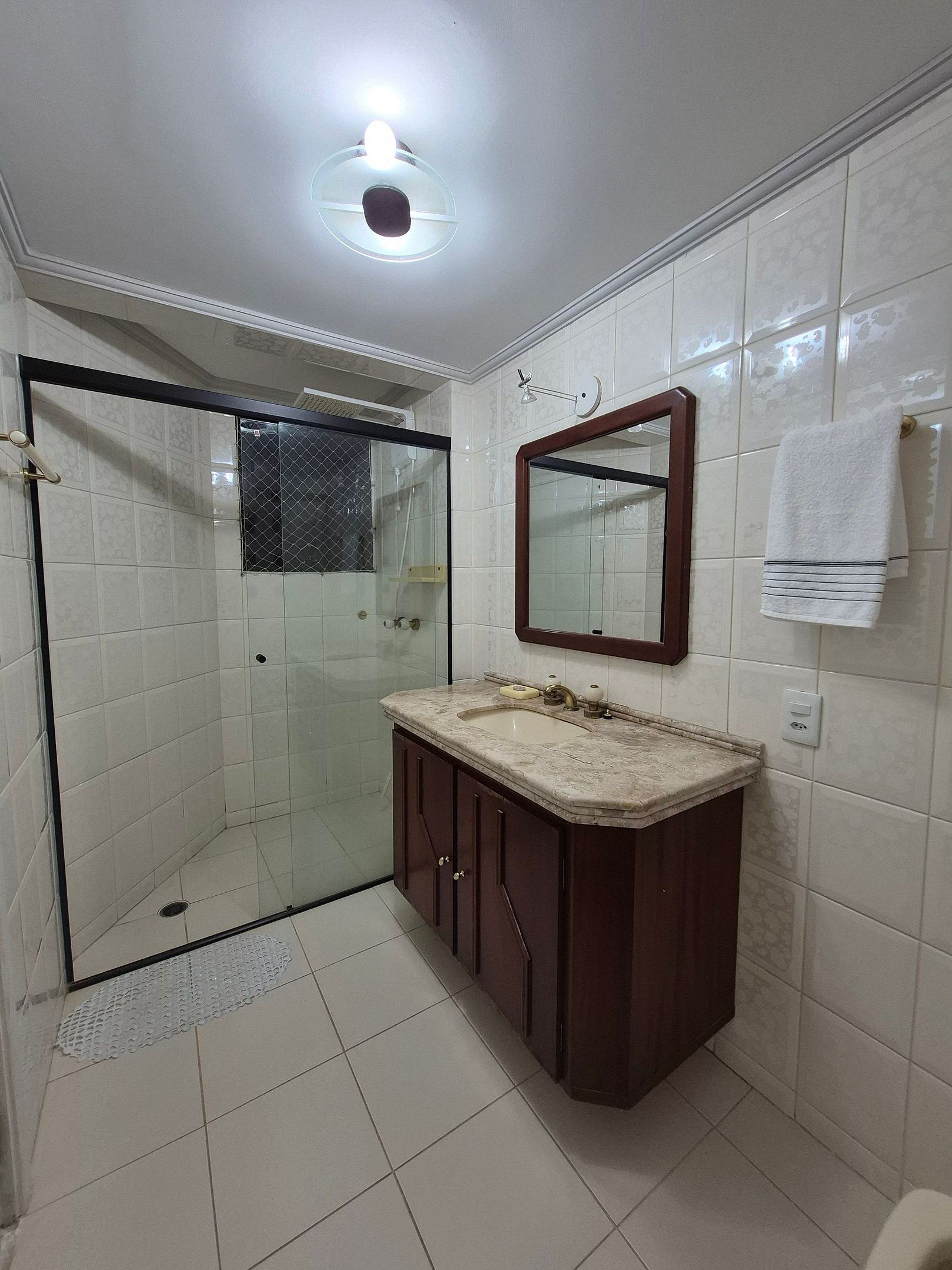 A bathroom with a glass shower enclosure, a vanity with a mirror, and a towel hanging on the wall.