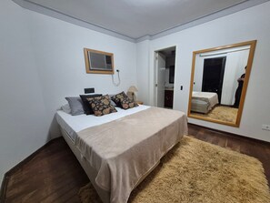 A bedroom with a bed, a mirror, a bedside table, and a door leading to a closet.