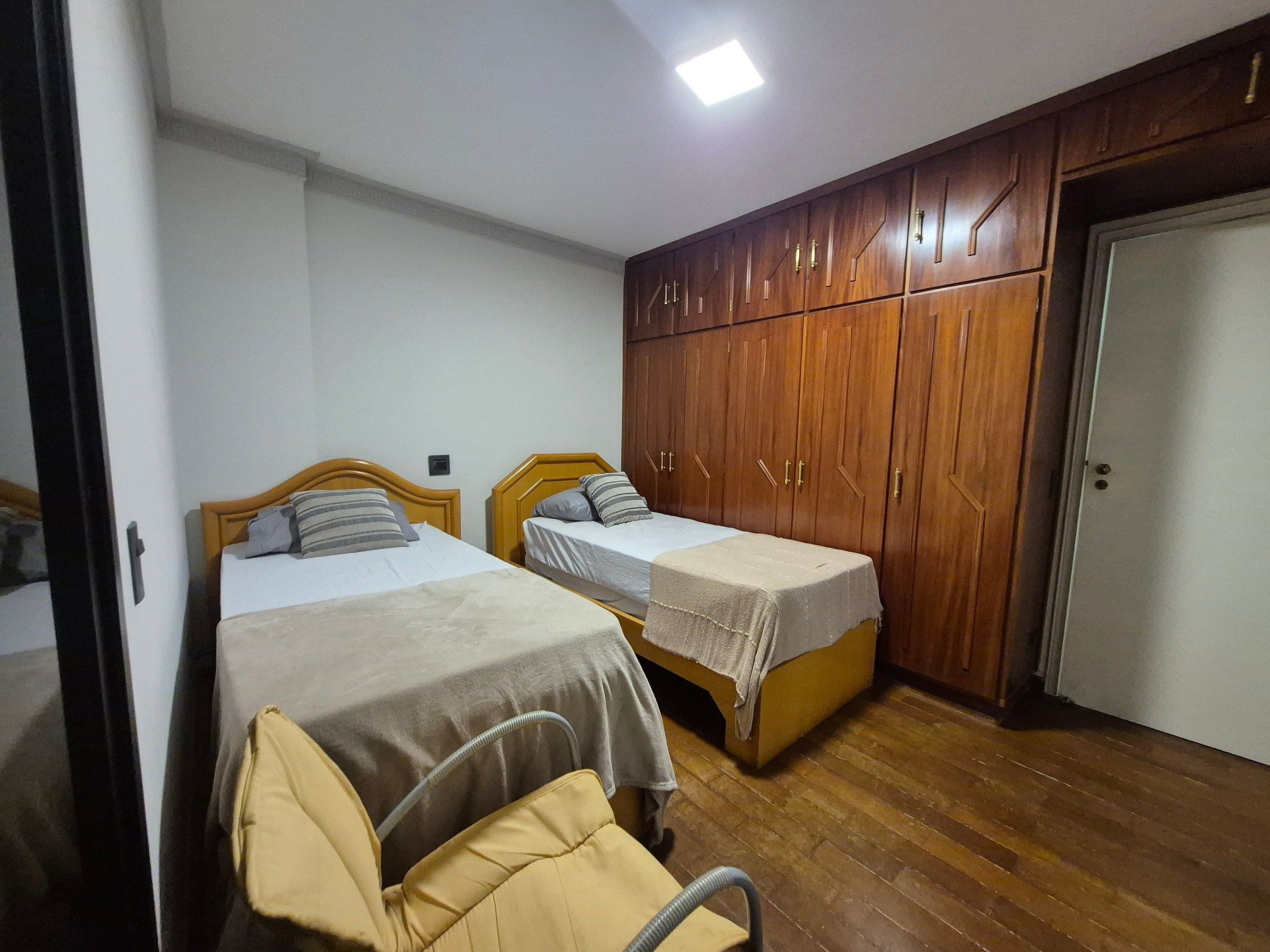 Une chambre avec deux lits simples, une armoire en bois et une porte.