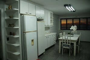 A kitchen with white cabinets, a refrigerator, a dining table with chairs, and a window with a view.