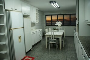 A kitchen with white cabinets, a dining table with chairs, a refrigerator, and a window with a view.