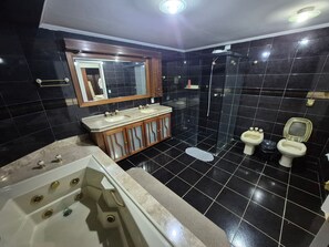A bathroom with a bathtub, two sinks, a glass-enclosed shower, and a toilet.