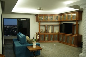 A living room with a blue sofa, a TV, wooden cabinets, and a view through a window.