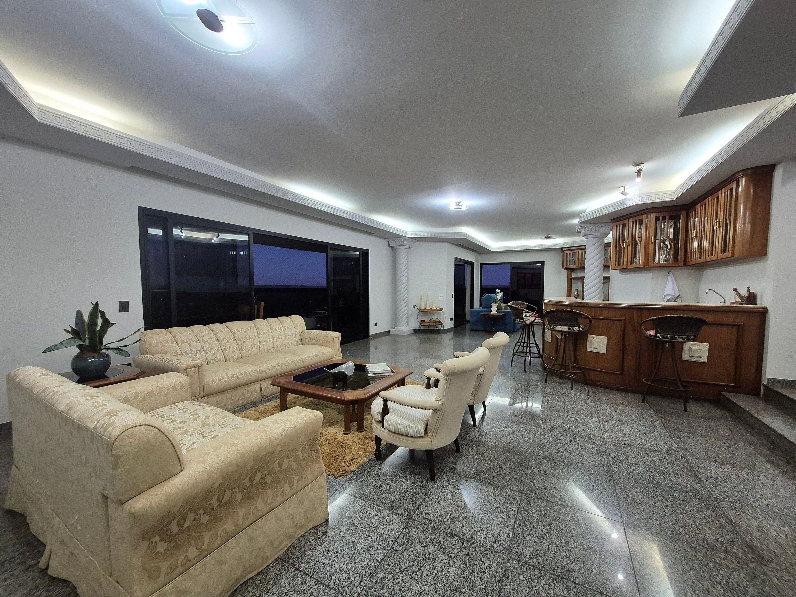 A spacious living area with a sofa, armchairs, a coffee table, and a kitchen area with wooden cabinets.