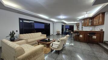 A spacious living area with a sofa, armchairs, a coffee table, and a kitchen area with wooden cabinets.
