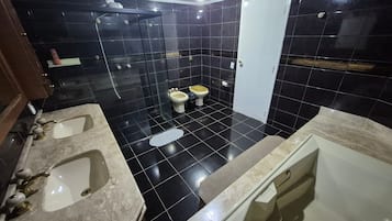 Une salle de bain avec deux lavabos, une baignoire, une douche et des toilettes.