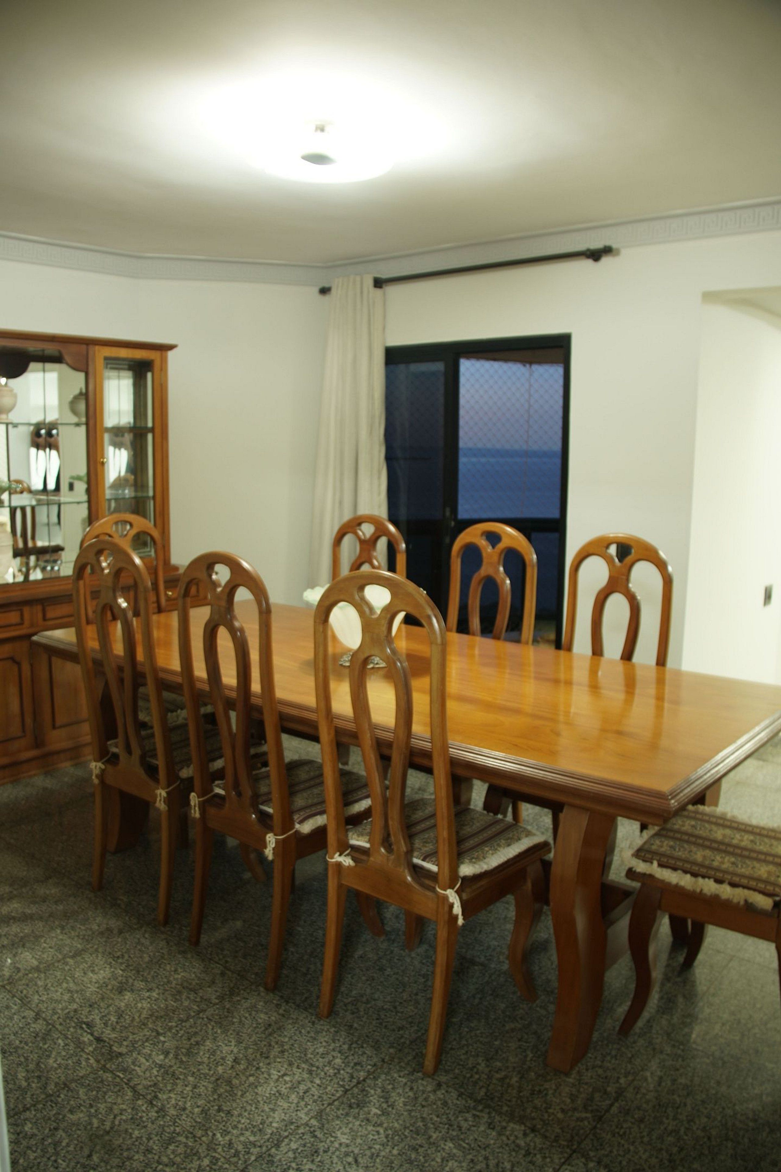A dining area with a wooden table and chairs, a cabinet with glass doors, and a view through a window.