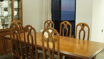 A dining area with a wooden table and chairs, a cabinet with glass doors, and a view through a window.