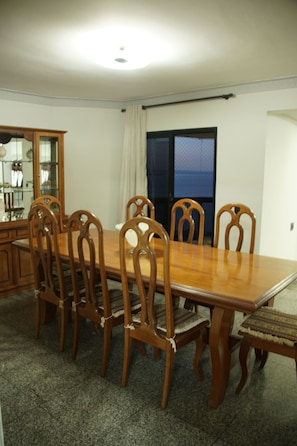 A dining area with a wooden table and chairs, a cabinet with glass doors, and a view through a window.