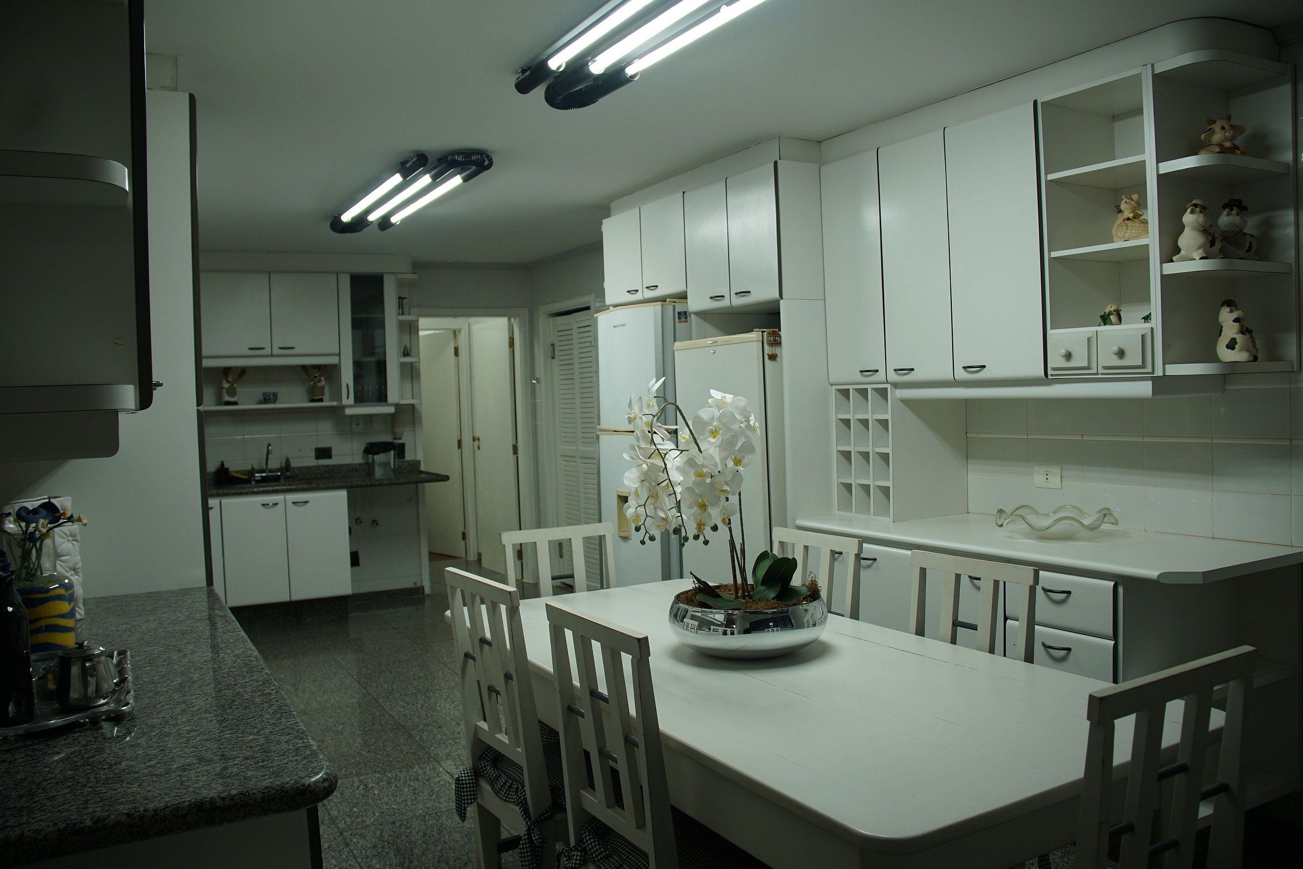 A kitchen with white cabinets, a dining table, chairs, and a flower vase.