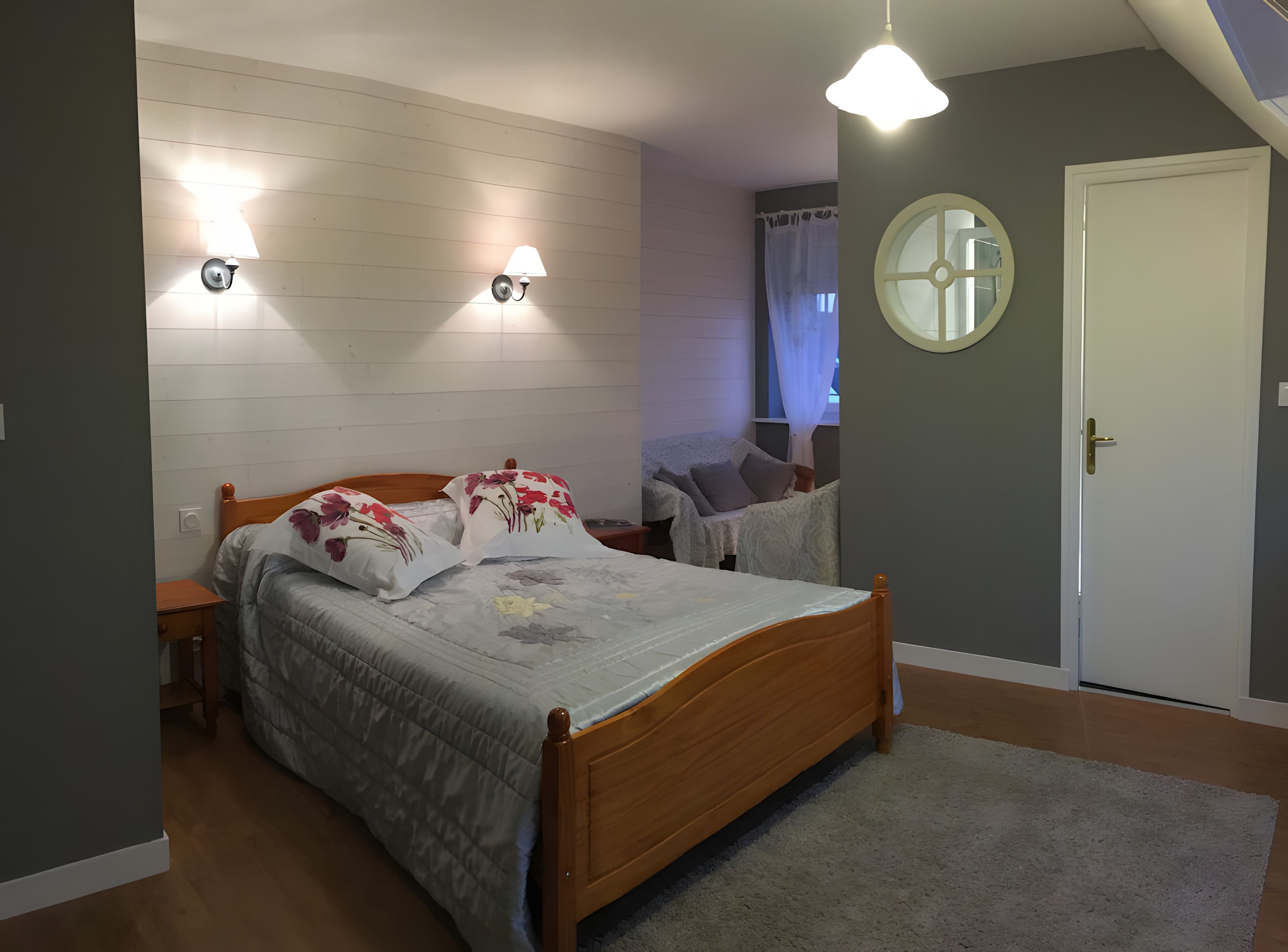 Ein Schlafzimmer mit einem hölzernen Bett, zwei Wandleuchten, einem runden Spiegel und einer Tür.