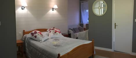 Een slaapkamer met een houten bed, twee wandlampen, een ronde spiegel en een deur.