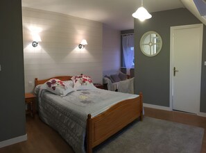 Une chambre à coucher avec un lit en bois, deux lampes fixées au mur, un miroir rond et une porte.