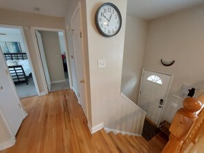 A staircase with a wooden handrail, a wall-mounted clock, and a door with a window.
