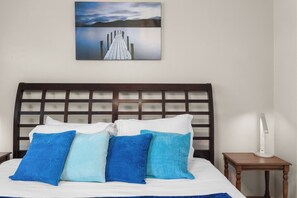 A bed with a wooden headboard, white bedding, and multiple blue and light blue pillows.