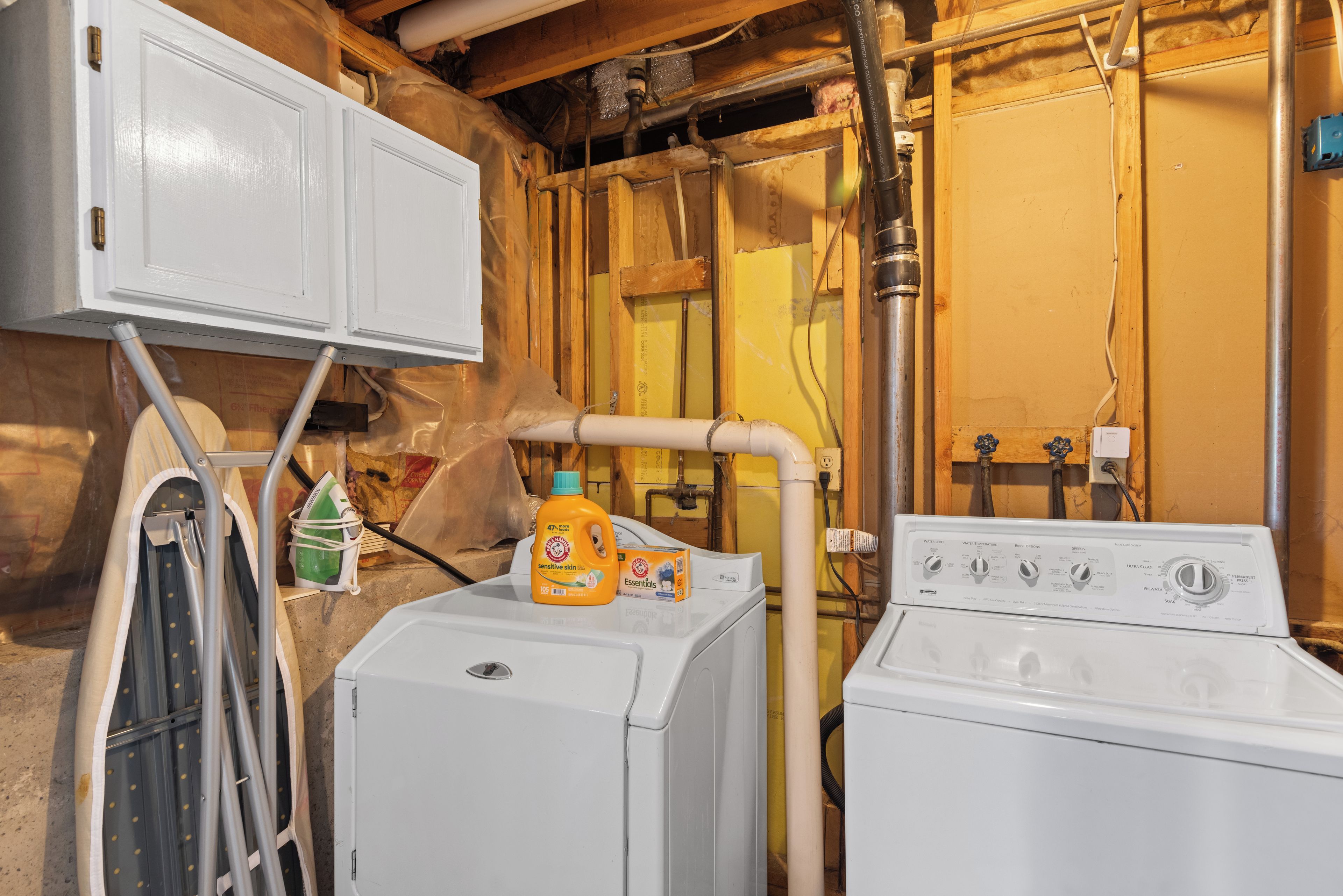 A laundry room with two washing machines, a water heater, and a utility room with wooden walls and insulation.