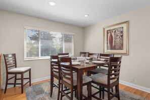 A dining room with a round table, six chairs, and a window with blinds.