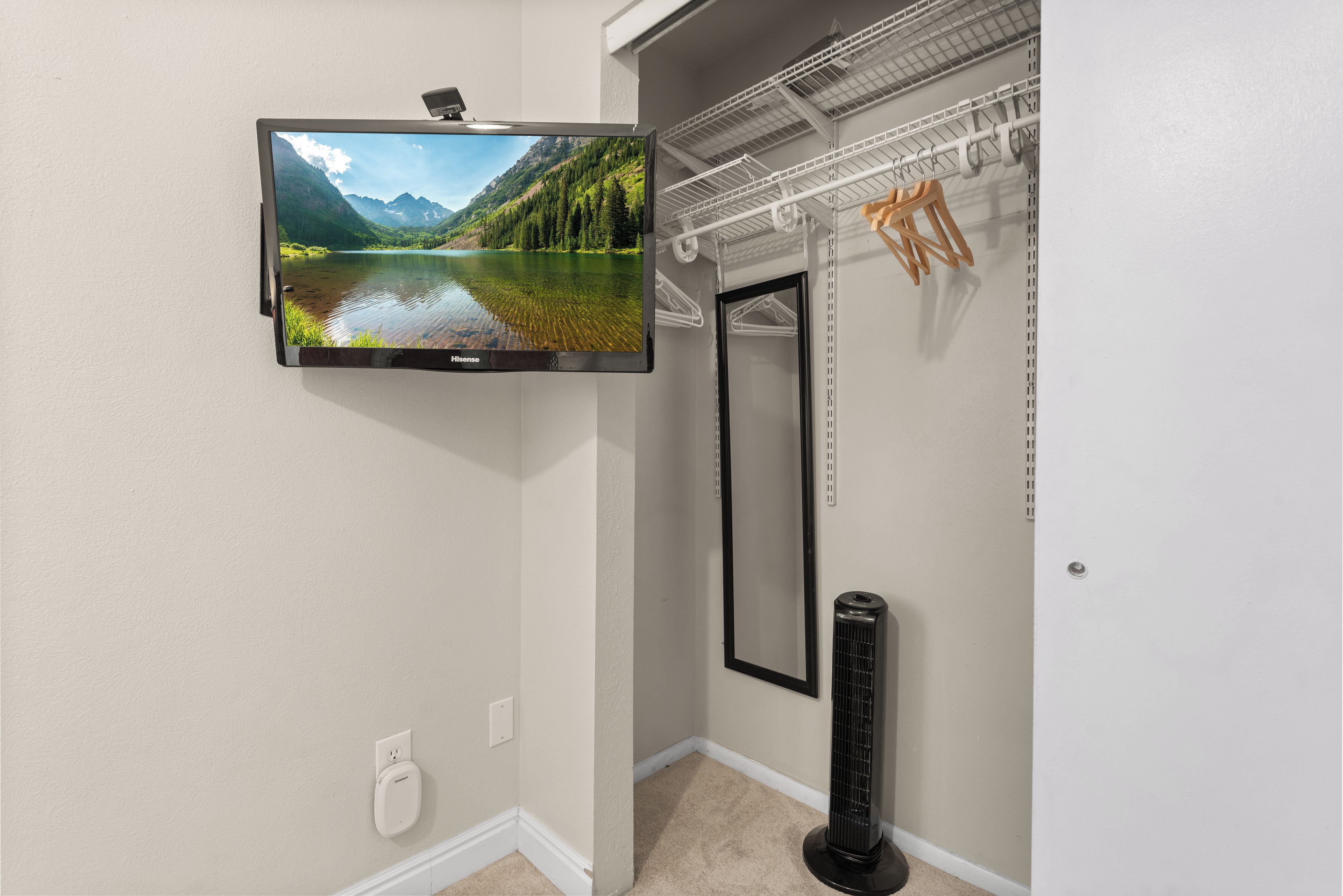 A flat-screen TV mounted on a wall, a mirror, a radiator, and a coat rack with hangers.
