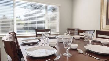Una mesa de comedor dispuesta con platos, vasos y cubiertos en una habitación con ventana y persianas.