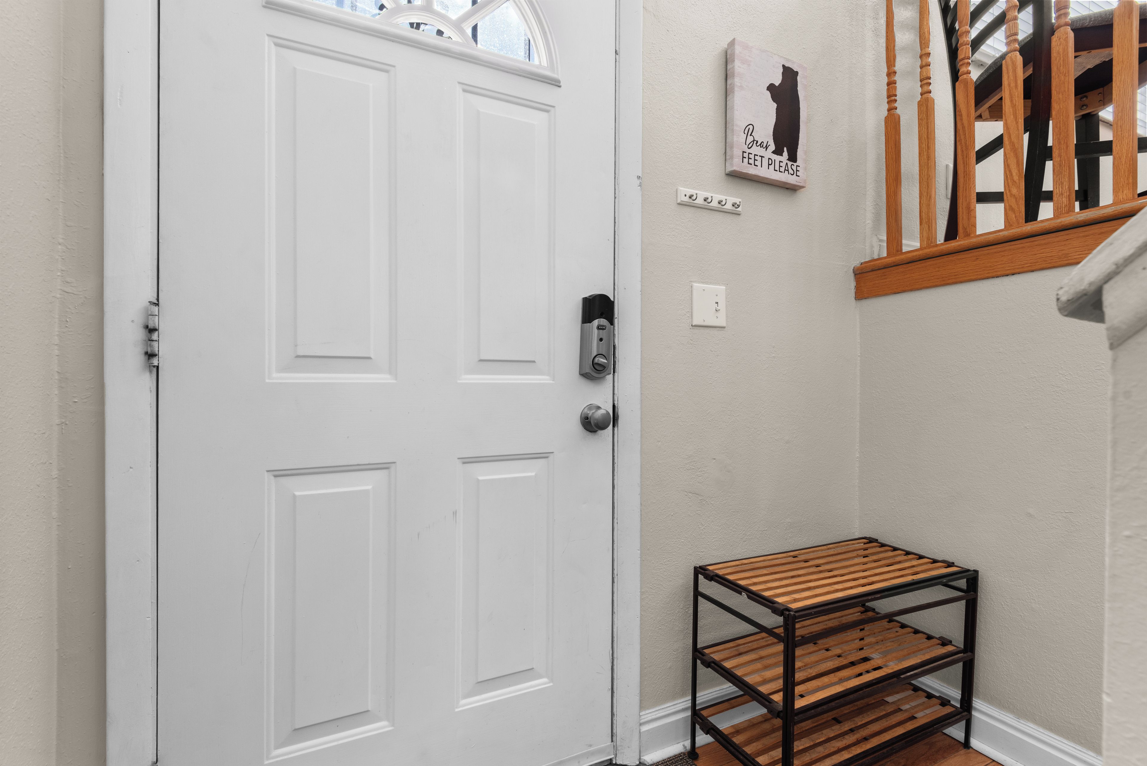 Une porte blanche dotée d’une serrure moderne, un petit banc en bois aux pieds métalliques et une enseigne fixée au mur, représentant la silhouette d’un ours et un texte.