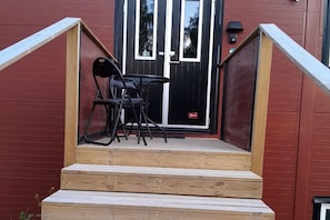 A wooden staircase leading to a black door with a glass panel, a small table with chairs, and a wall-mounted light fixture.