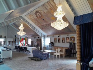 Ein geräumiger Raum mit hoher Decke, Kronleuchtern, einem langen Tisch und mehreren Stühlen.
