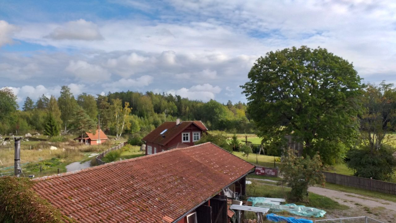 Ein ländliches Haus mit rotem Dach, umgeben von Bäumen und einem klaren Himmel.