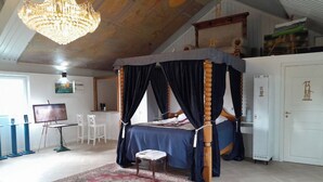 Un lit à baldaquin à quatre poteaux, agrémenté d’un tapis aux motifs rouges et beiges, d’une porte blanche et d’un plafond orné d’un lustre.