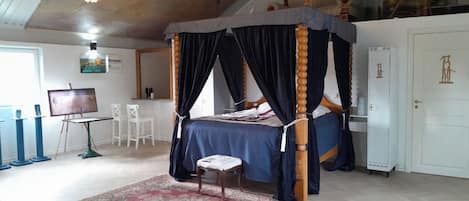A four-poster canopy bed with a red and beige patterned rug, a white door, and a ceiling with a chandelier.