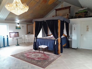 Una cama con dosel sobre cuatro columnas, un tapete rojo y beige con diseño, una puerta blanca y un techo con candelabro.
