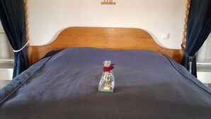 Ein Bett mit einem Holz-Kopfteil, einer blauen Bettdecke und einer kleinen Geschenkverpackung mit roter Schleife auf dem Bett.