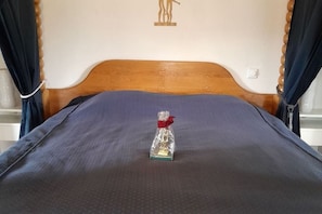 Ein Bett mit einem Holz-Kopfteil, einer blauen Bettdecke und einer kleinen Geschenkverpackung mit roter Schleife auf dem Bett.