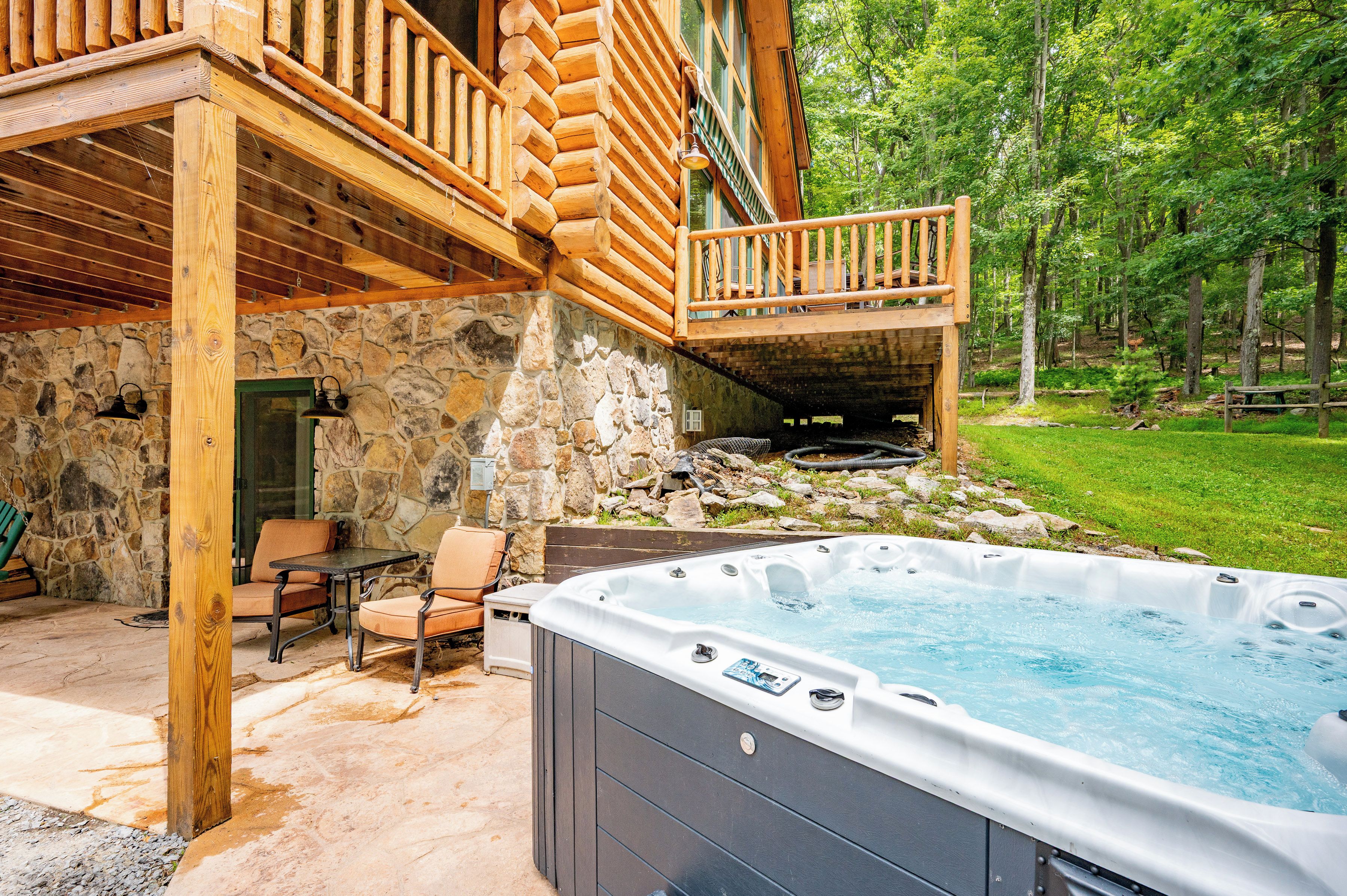 A wooden cabin with a stone exterior, a hot tub, outdoor seating, and a stone fireplace.