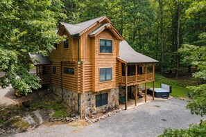 A log cabin with a stone foundation, a balcony, and a hot tub.
