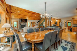 A spacious living area with a large wooden dining table, leather chairs, and a chandelier.