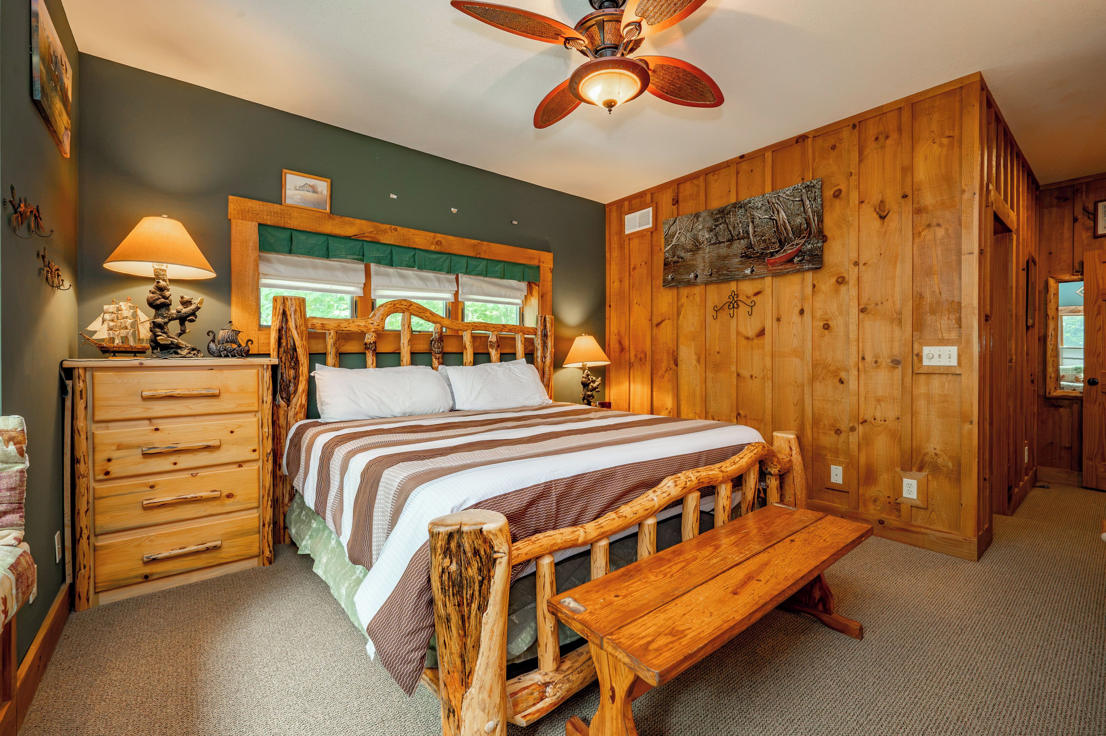 A bedroom with a wooden bed, a wooden bench, a dresser, and a ceiling fan.