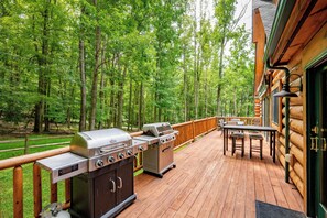 A deck with a grill and outdoor furniture, surrounded by a forest.