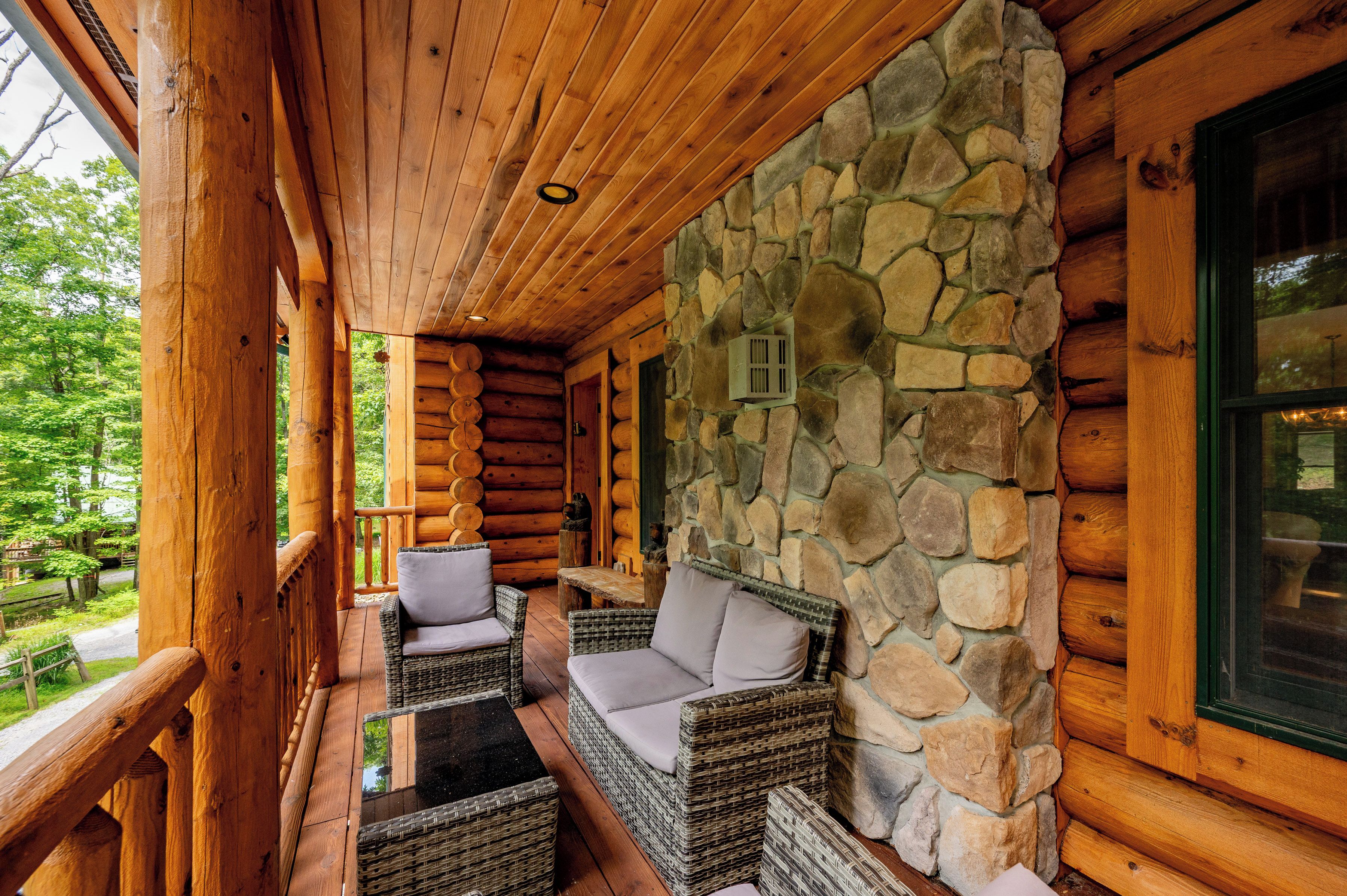 A log cabin with a stone wall, wicker furniture, and a wooden ceiling.