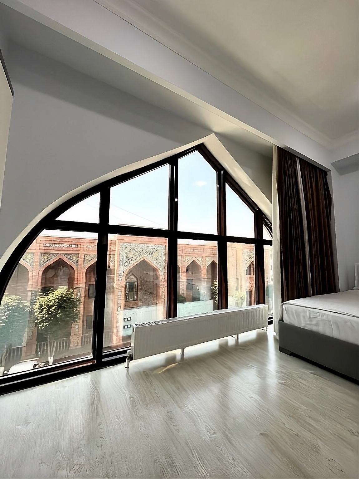 A hotel room with a large arched window, a bed, and a radiator.