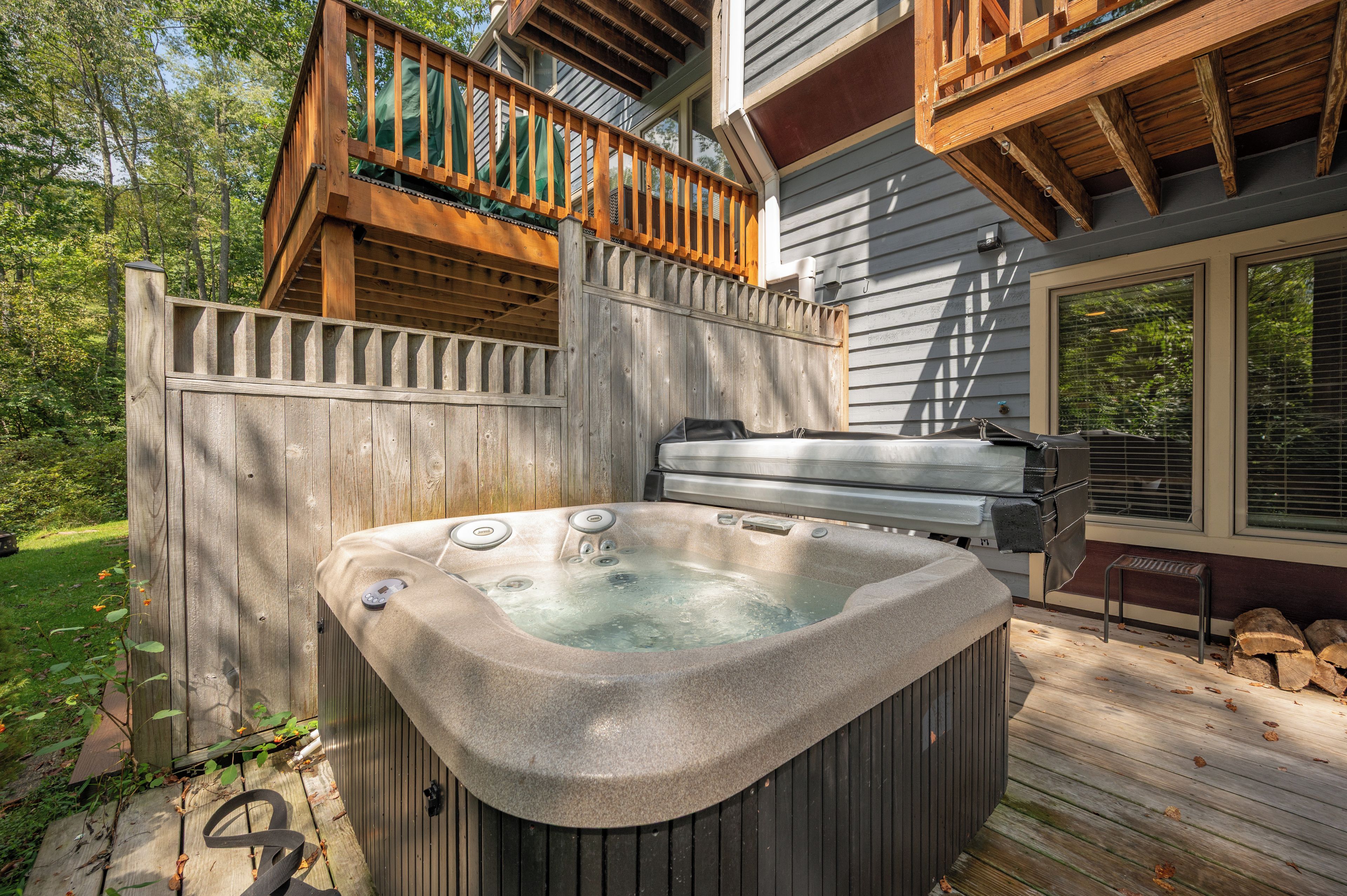 Un bain à remous sur une terrasse en bois, avec une clôture en bois et une maison en arrière-plan.