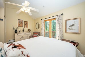 A bedroom with a bed, a dresser, a chair, a ceiling fan, a window with curtains, and wall art. - New! Ski In/Out Home w/ Hot Tub! (McHenry)